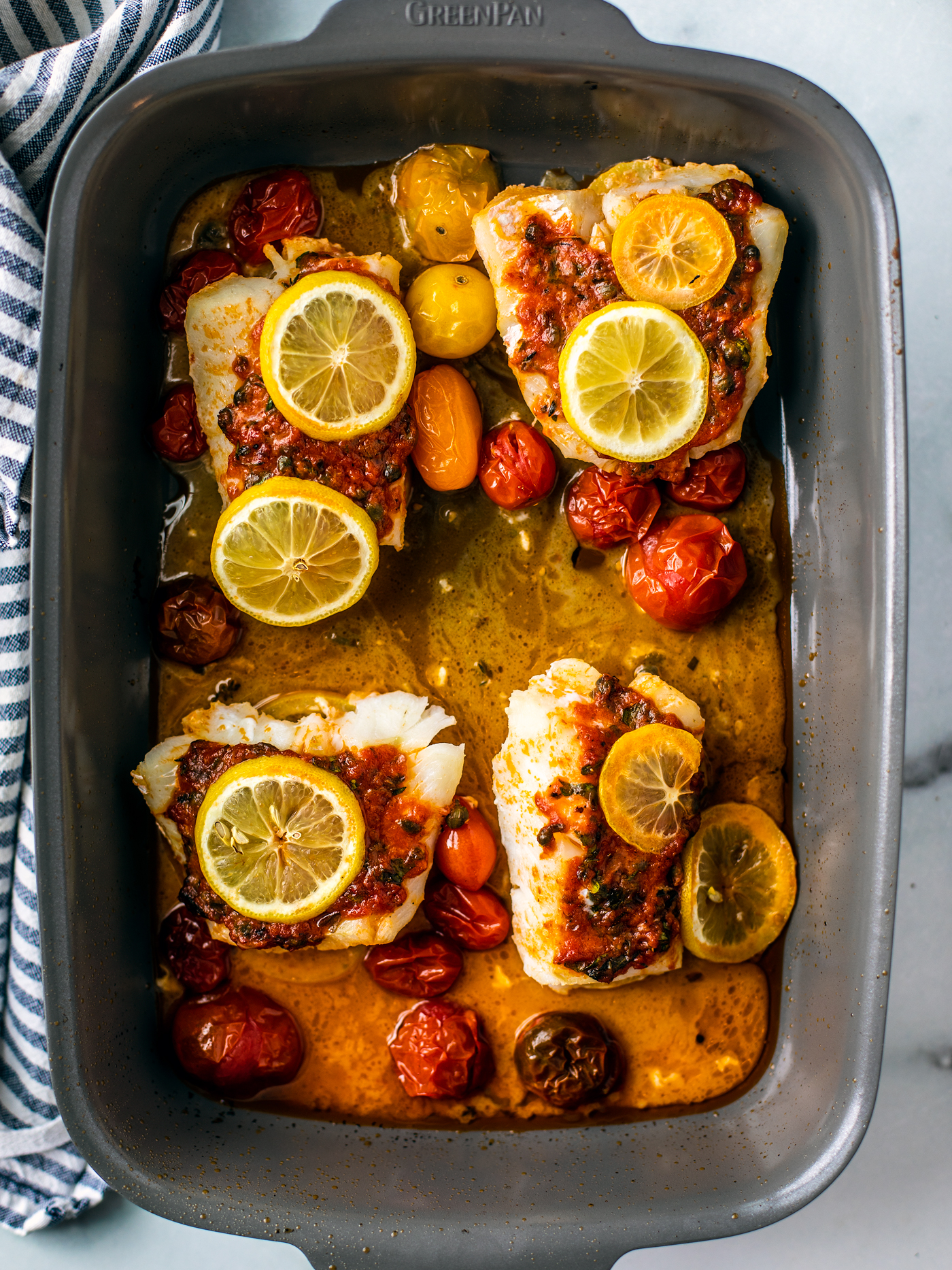 Baking dish with four cooked cod fillets and tomatoes with pan sauce.