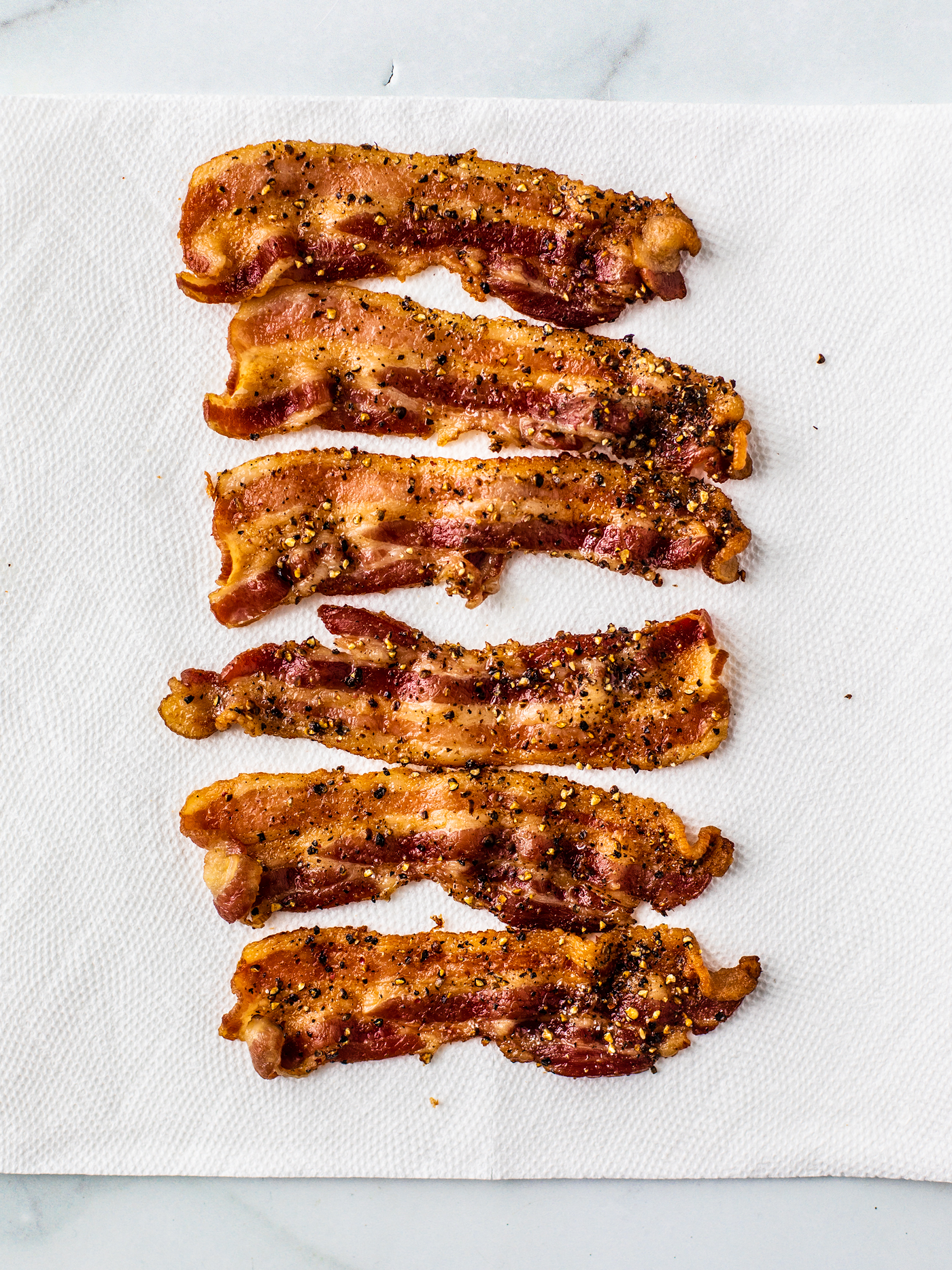 Paper towel with cooked bacon spied with cracked black pepper.