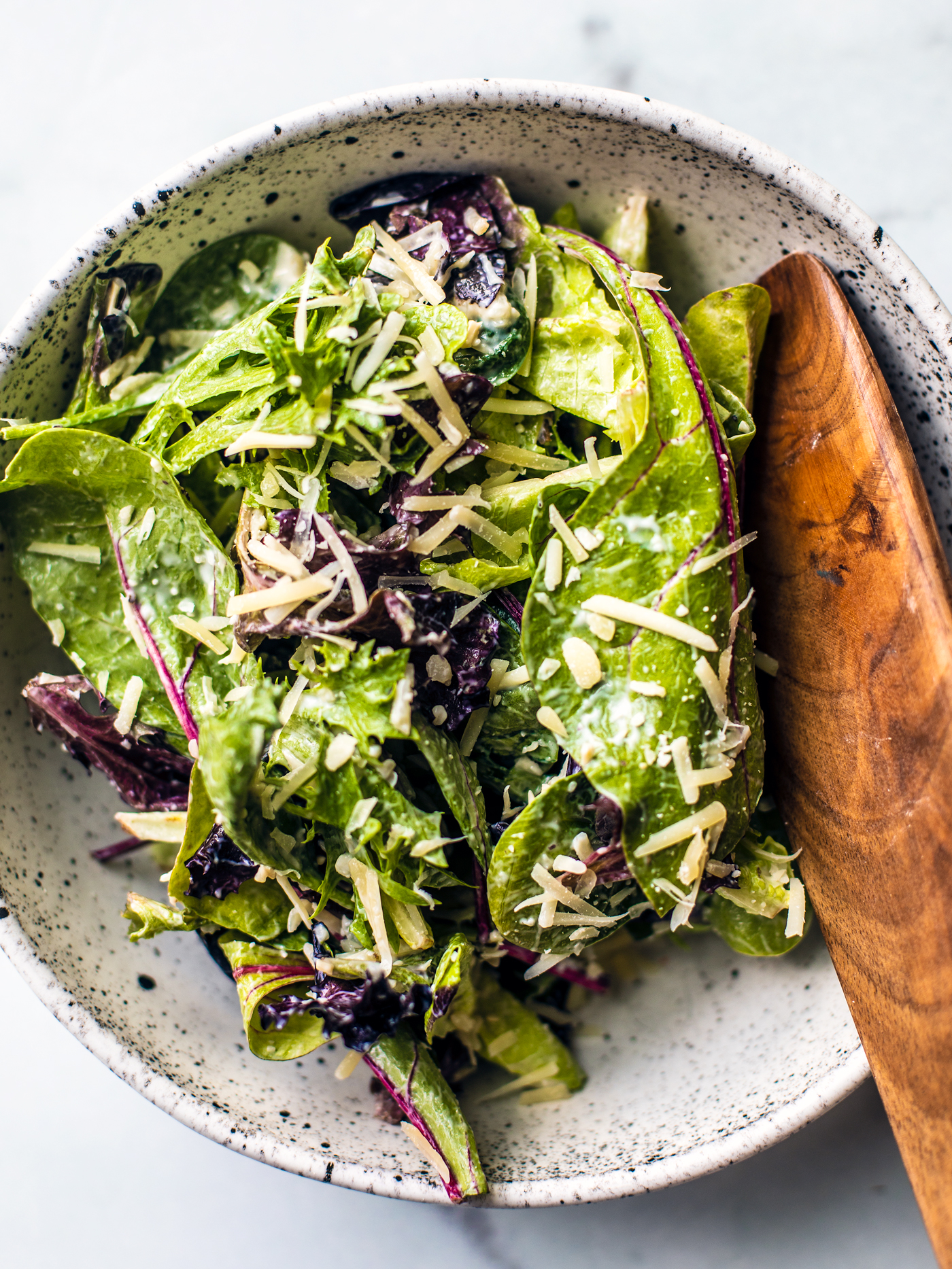 Bowl of mixed greens dressed in Caesar dressing and a sprinkle of parmesan cheese.