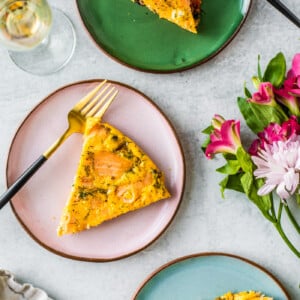 Slices of quiche on colorful pottery plates with flowers and a glass of champagne.
