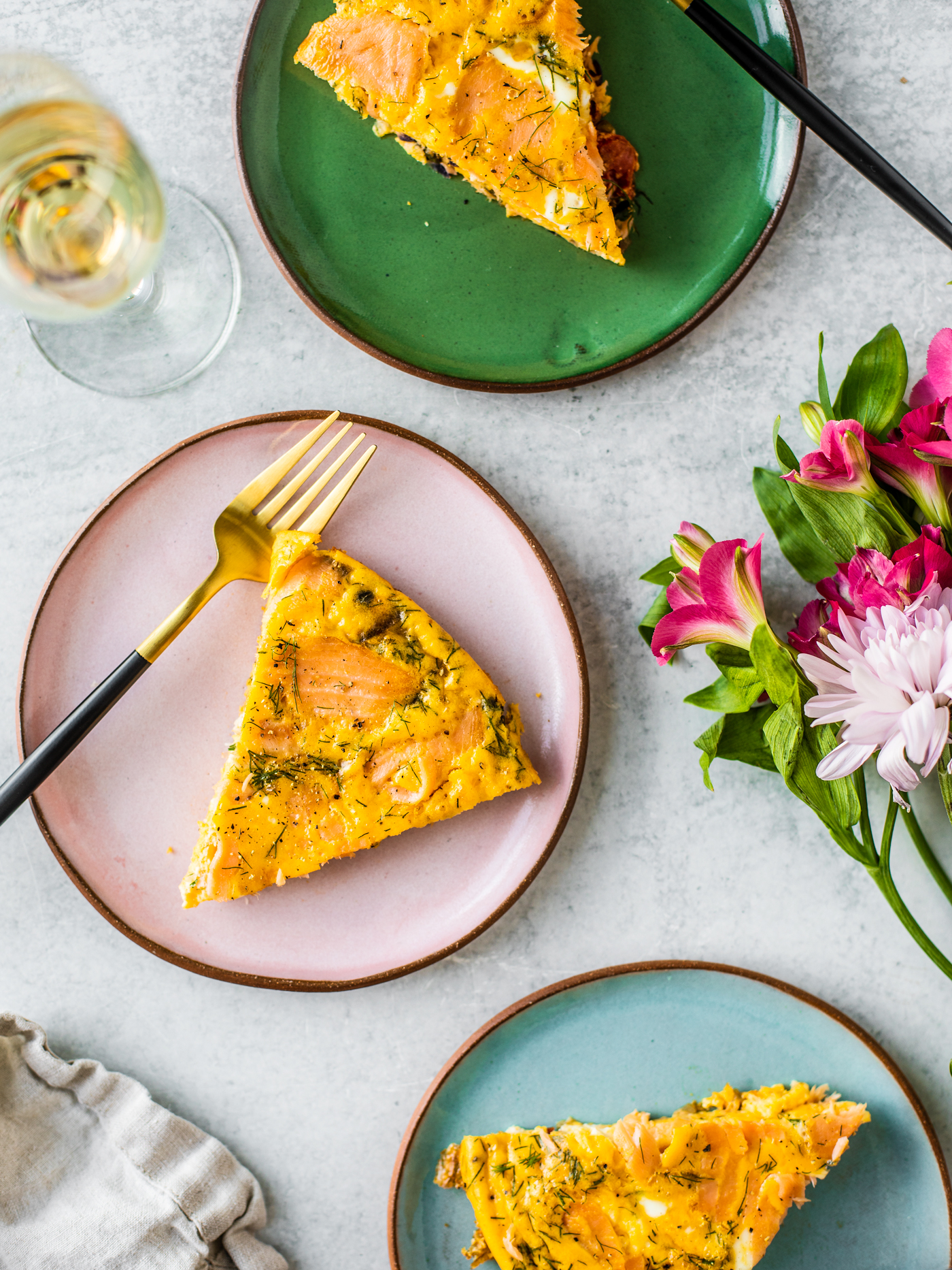 Slices of quiche on colorful pottery plates with flowers and a glass of champagne.