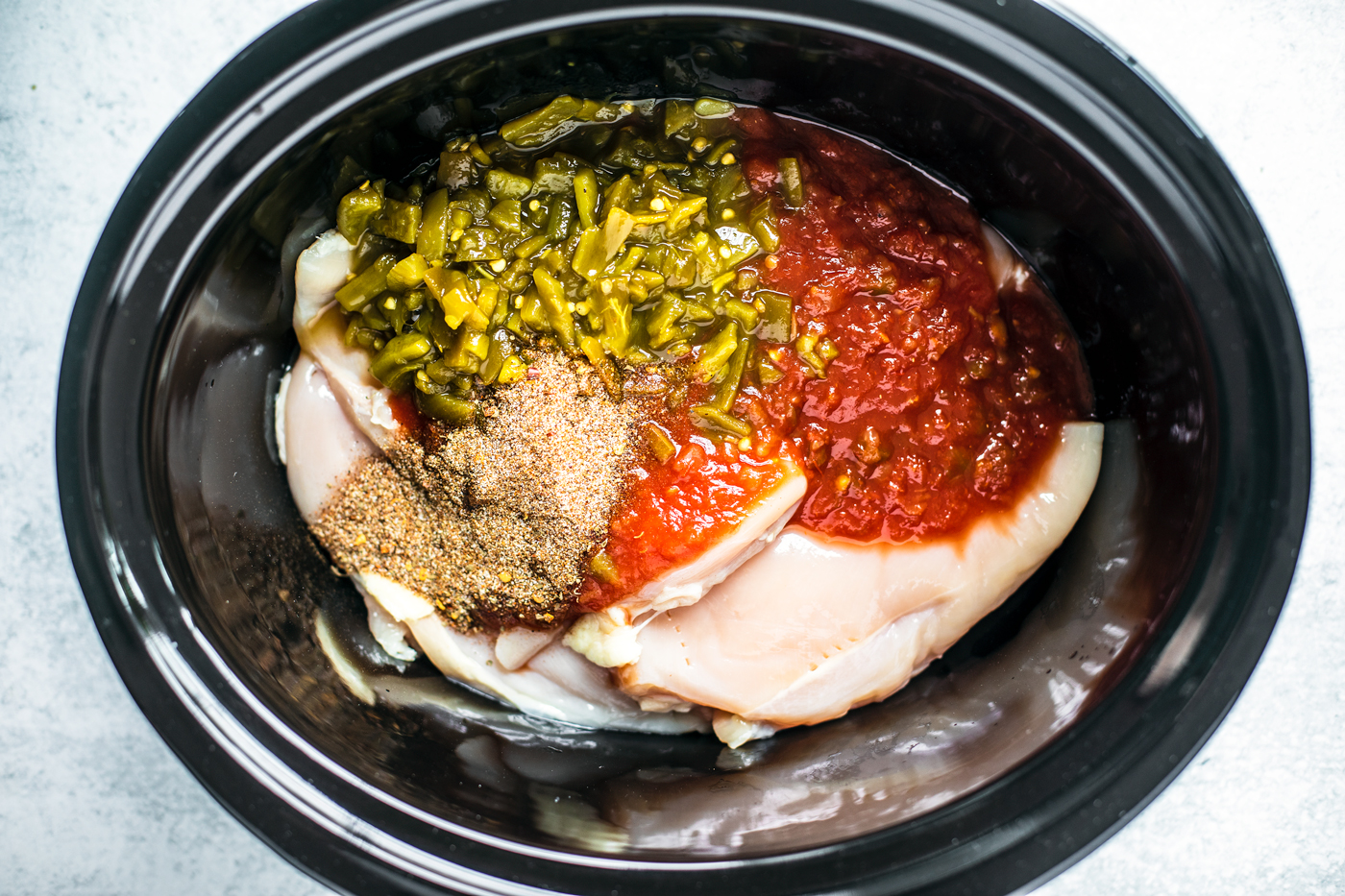 Chicken breasts in a slow cooker with salsa, green chiles, and taco seasoning.