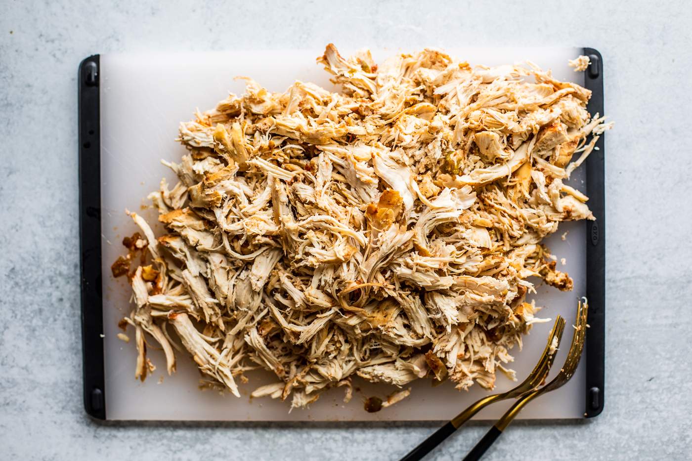 Shredded chicken on a cutting board with two forks.
