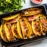 Cast iron baking dish filled with cheesy baked shredded chicken tacos.