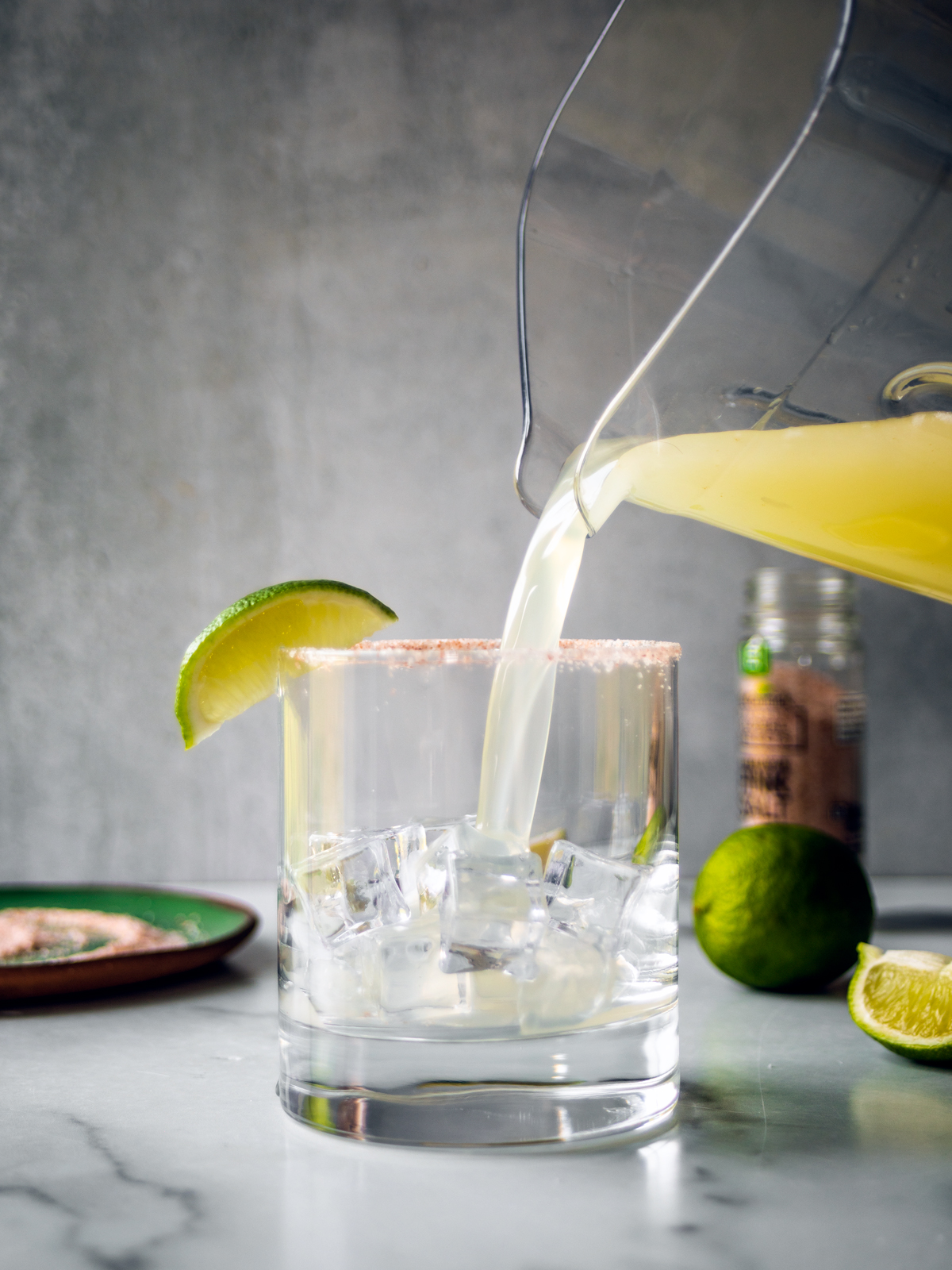 Salt-rimmed glass of ice with margarita being poured into it.