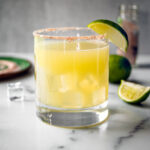 Glass of margarita with salt rim and lime wedge.