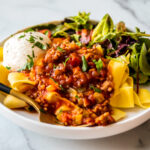 Side shot close up of sausage pasta sauce spooned over pappardelle with a hunk of burrata and a side salad.