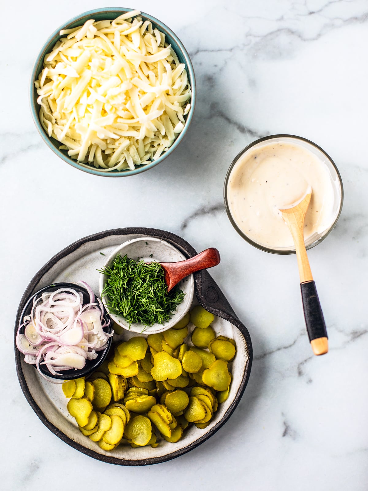 Ingredients for dill pickle pizza on a white marble background.