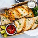 Shrimp quesadillas on a sheet pan with dipping bowls of sour cream and salsa.
