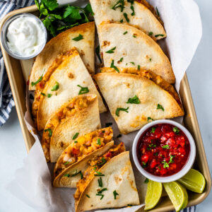 Shrimp quesadillas on a sheet pan with dipping bowls of sour cream and salsa.