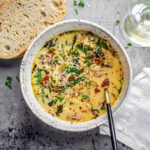Bowl of chicken florentine soup next to a hunk of fresh bread and a glass of wine.
