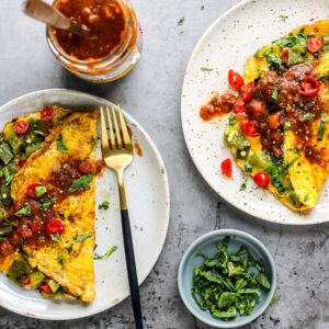 Two plates of omelets topped with salsa, a jar of salsa off to the side.