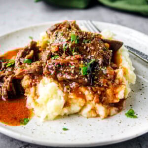 Plate of mashed potatoes smothered in beef bourguignon, gravy, and garnished with parsley, with a green napkin in the background.