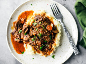 Plate of mashed potatoes smothered in beef bourguignon, gravy, and garnished with parsley.