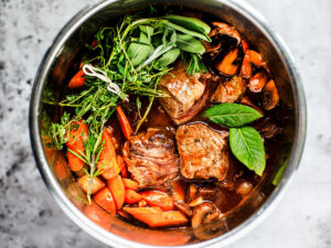 Beef chuck chunks nestled into the Instant Pot with carrots, bay leaves, and herbs.
