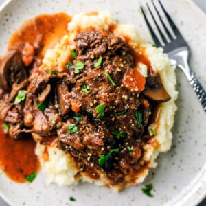 Plate of mashed potatoes smothered in beef bourguignon, gravy, and garnished with parsley.