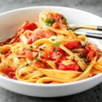 Side shot of white bowl of twirled clam pasta.