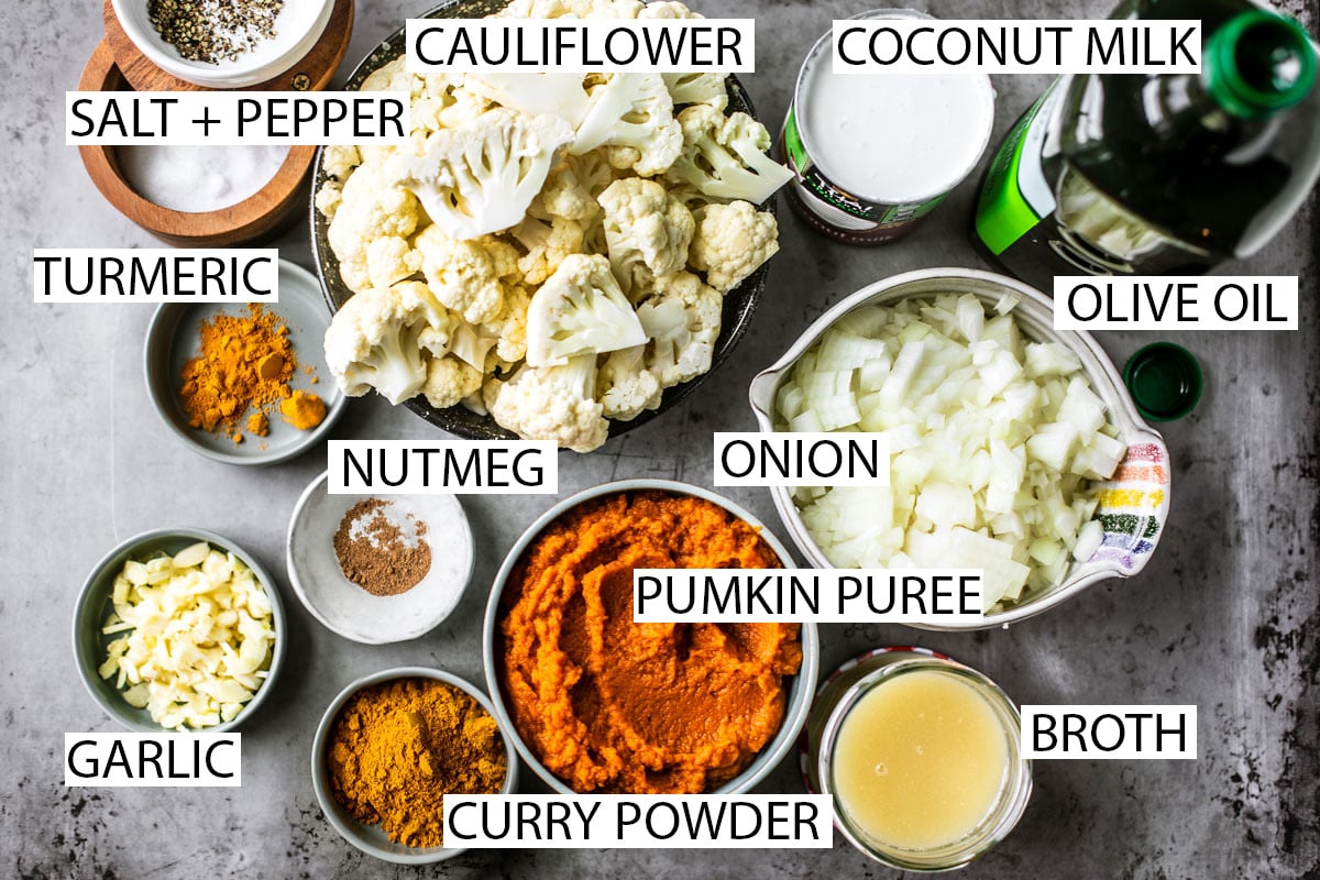 Ingredients laid out over background: salt + pepper, turmeric, garlic, curry powder, nutmeg, cauliflower, olive oil, coconut milk, onions, pumpkin puree, and broth.