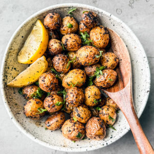 Crispy air fryer baby potatoes in a white serving bowl with a wooden spoon.
