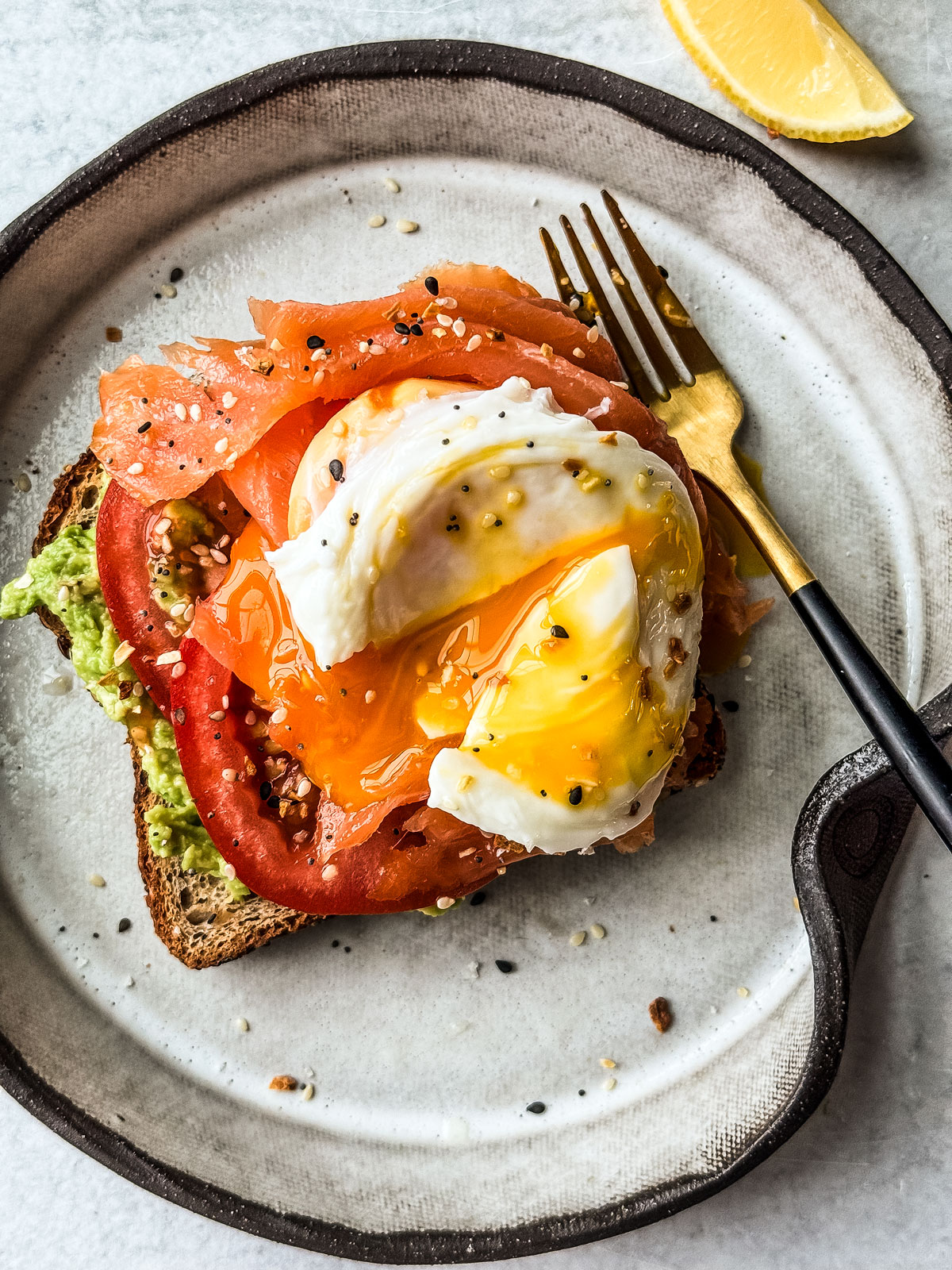 Toast smothered in avocado and topped with tomato and a broken poached egg.