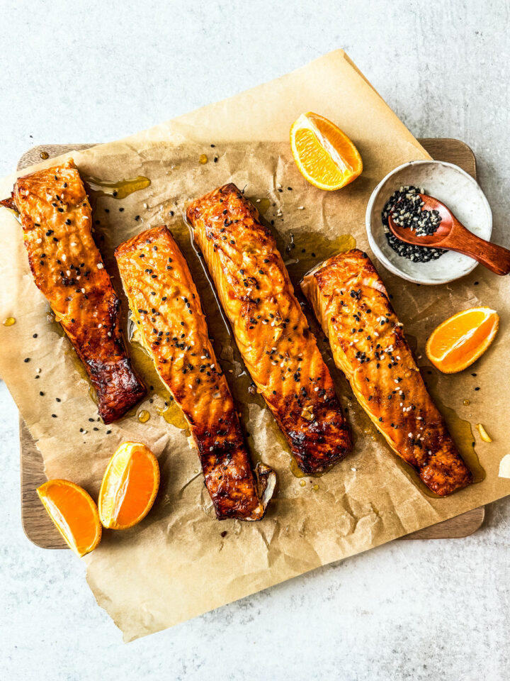 Salmon slathered with a honey orange glaze on a serving board with orange wedges.