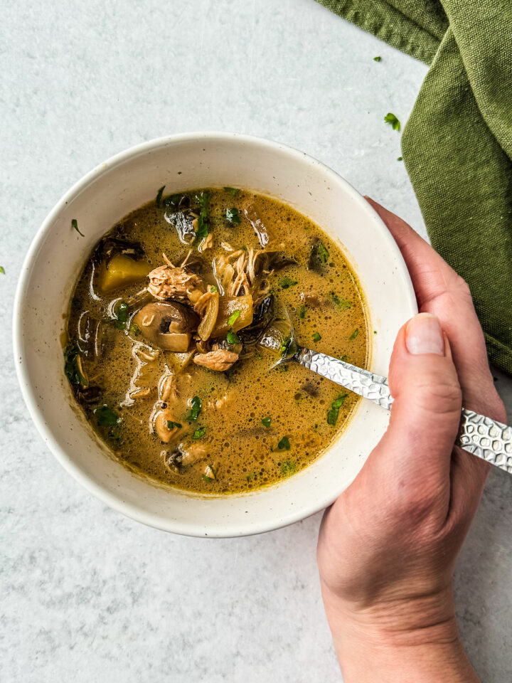 Hand holding bowl of chicken marsala soup.