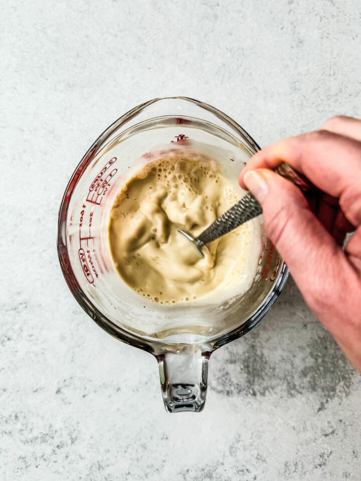 Heavy cream being whisked in a glass measuring cup.