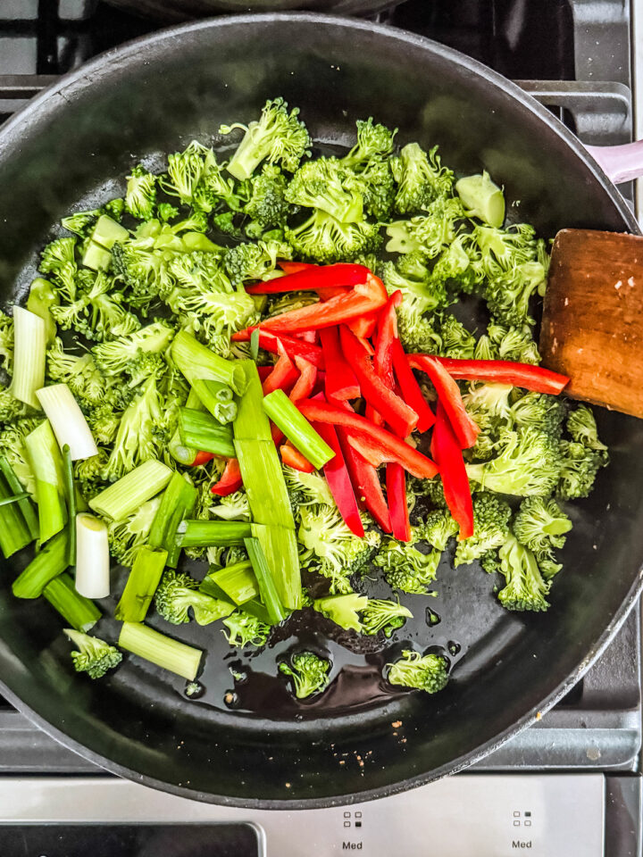 Broccoli, scallions, and red peppers in a cast iron pan.