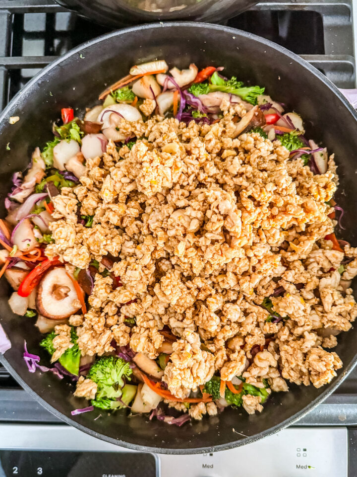 Ground turkey added to vegetables in a cast iron skillet.