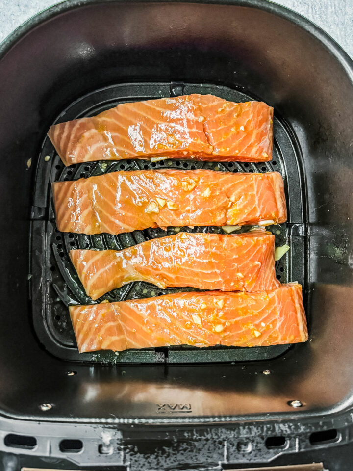 Uncooked salmon fillets in an air fryer basket.