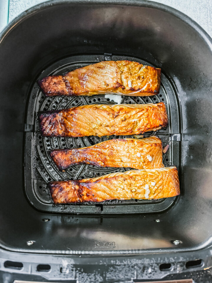 Cooked salmon fillets in an air fryer basket.