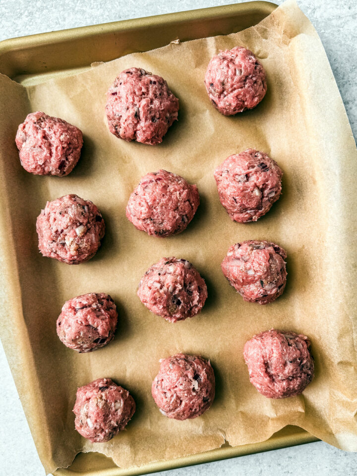 Ground turkey meatballs rolled and on a parchment-lined baking sheet.