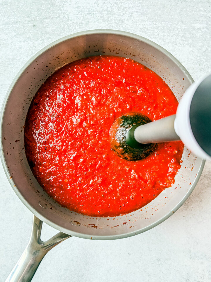 Immersion blender blending the marinara sauce in a pan.