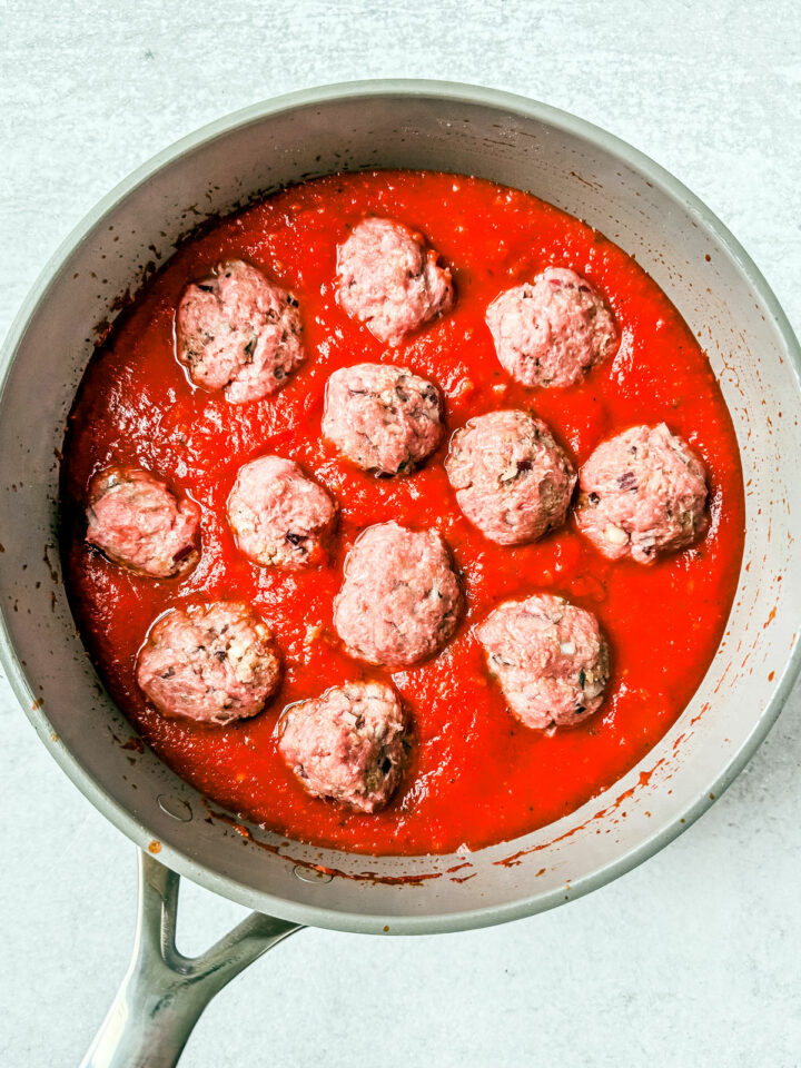 Uncooked turkey meatballs in a pan with marinara sauce.
