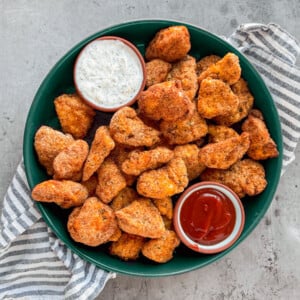 Green serving bowl of chicken nuggets with dipping sauces.