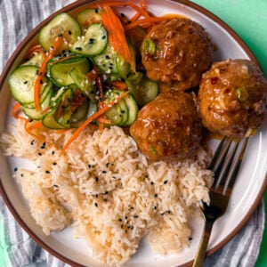 Plate of baked turkey meatballs glazed with hot honey, rice, and cucumber salad.