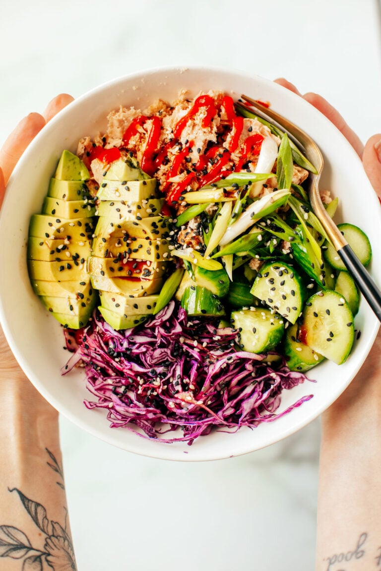 Hands holding up a bowl of canned tuna with various veggies.