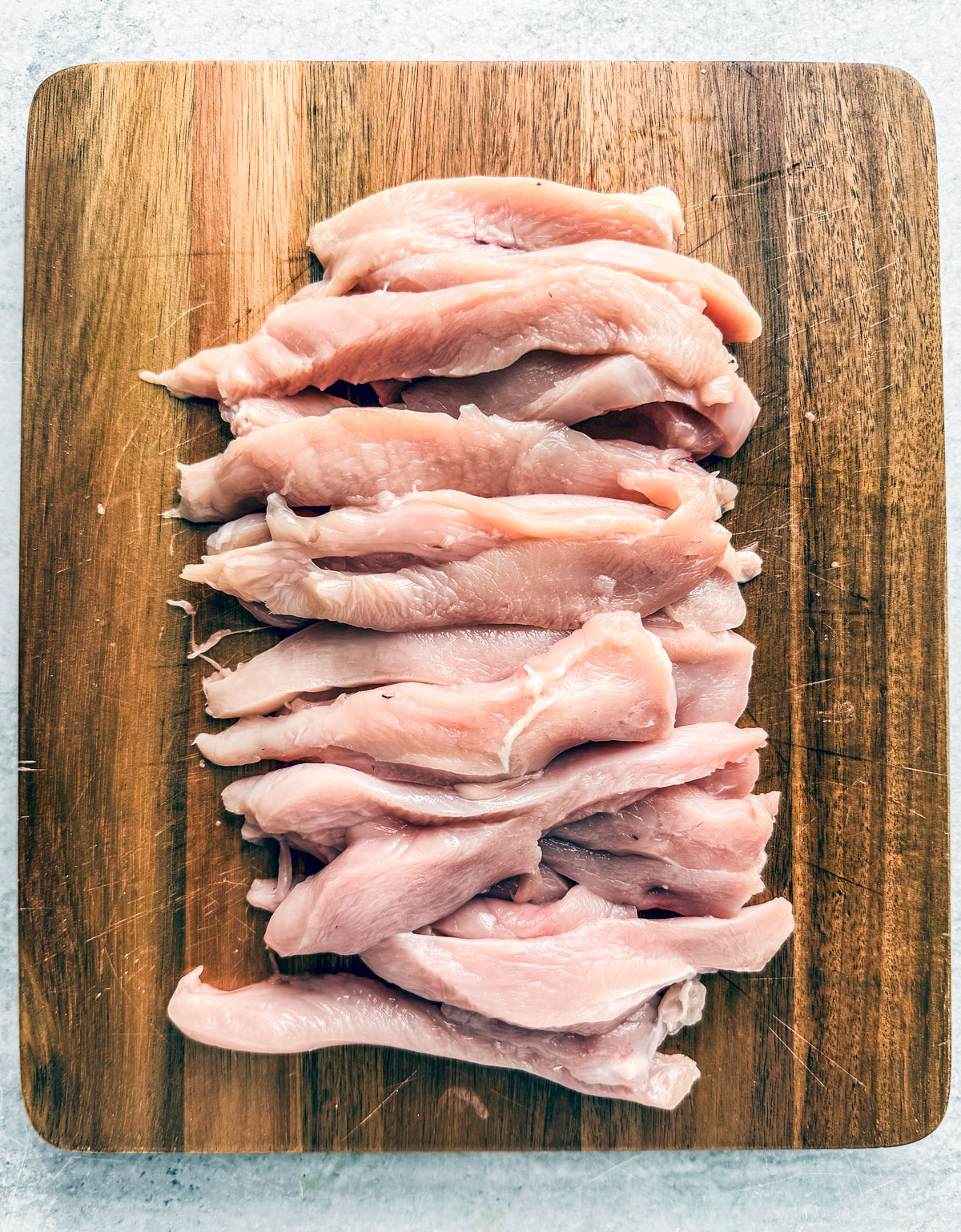 Chicken breasts cut into strips on a cutting board.