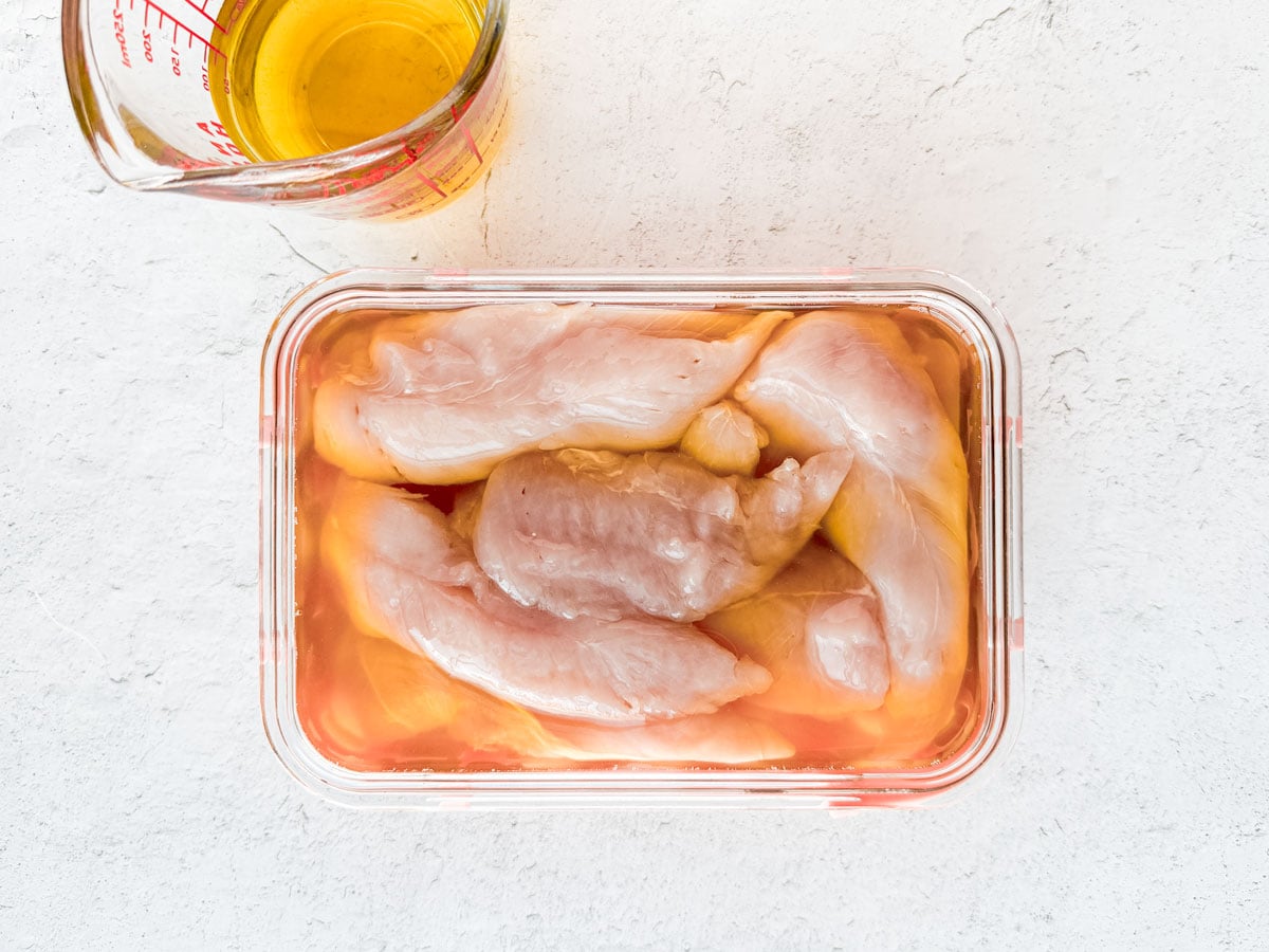 Chicken tenders in a container of pickle brine.