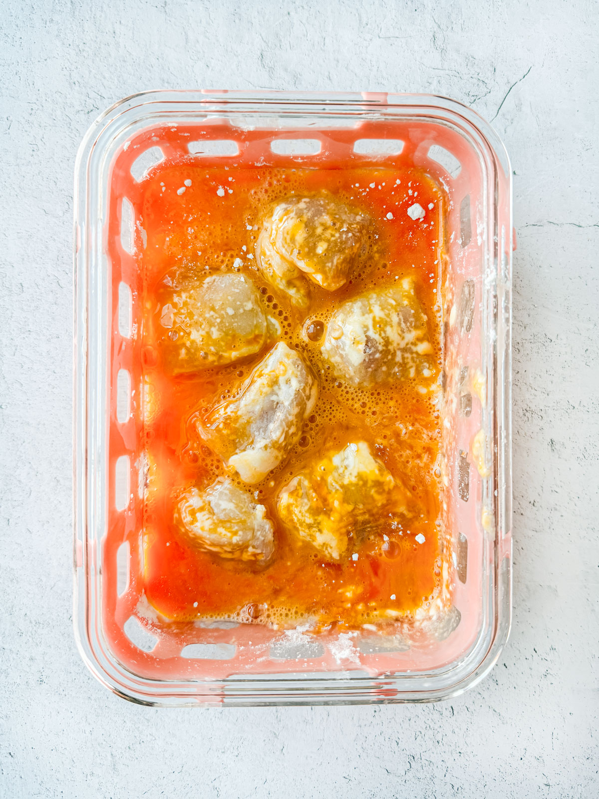 Flour-dusted chicken nuggets in a container of egg wash.