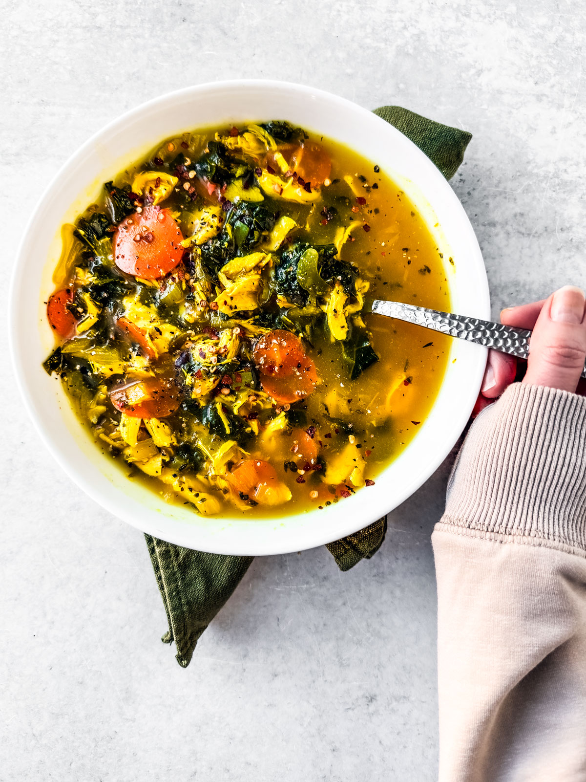 Hand spooning into a bowl of chicken soup with turmeric and ginger.