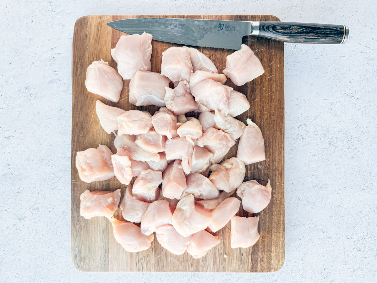 Cubes of uncooked chicken on a cutting board with a knife.