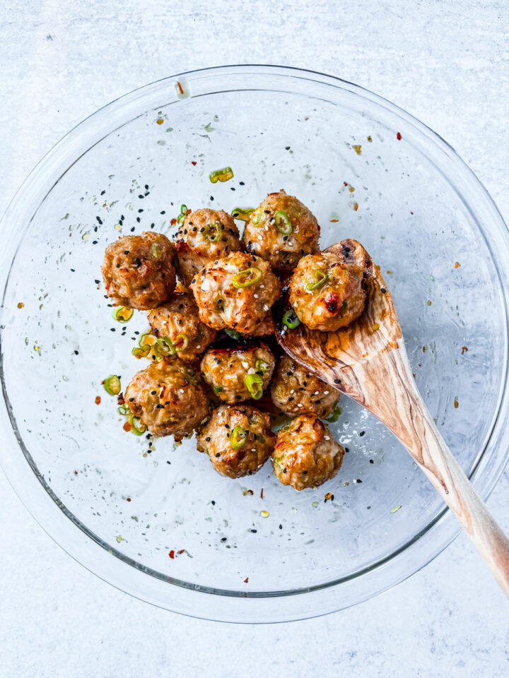 Meatballs in a mixing bowl tossed in honey glaze. 