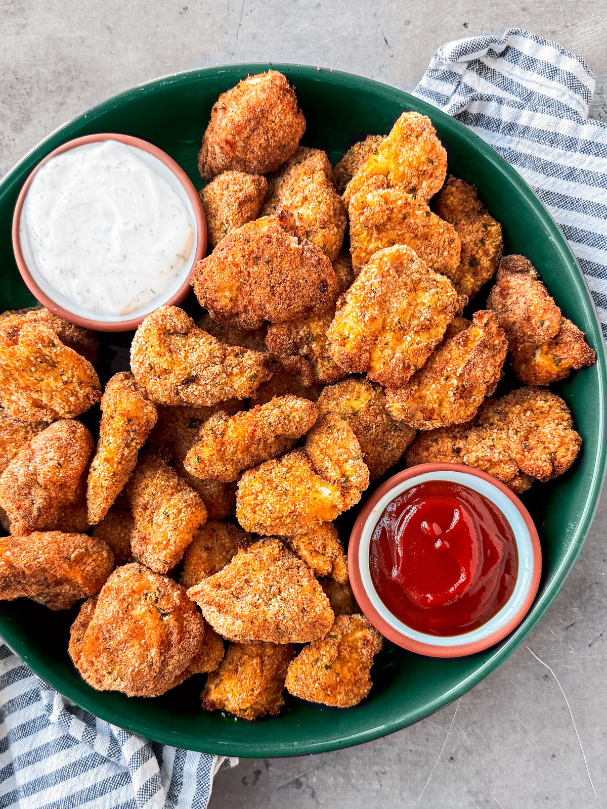 Air fryer chicken nuggets in a green serving bowl with a side of ranch and ketchup.