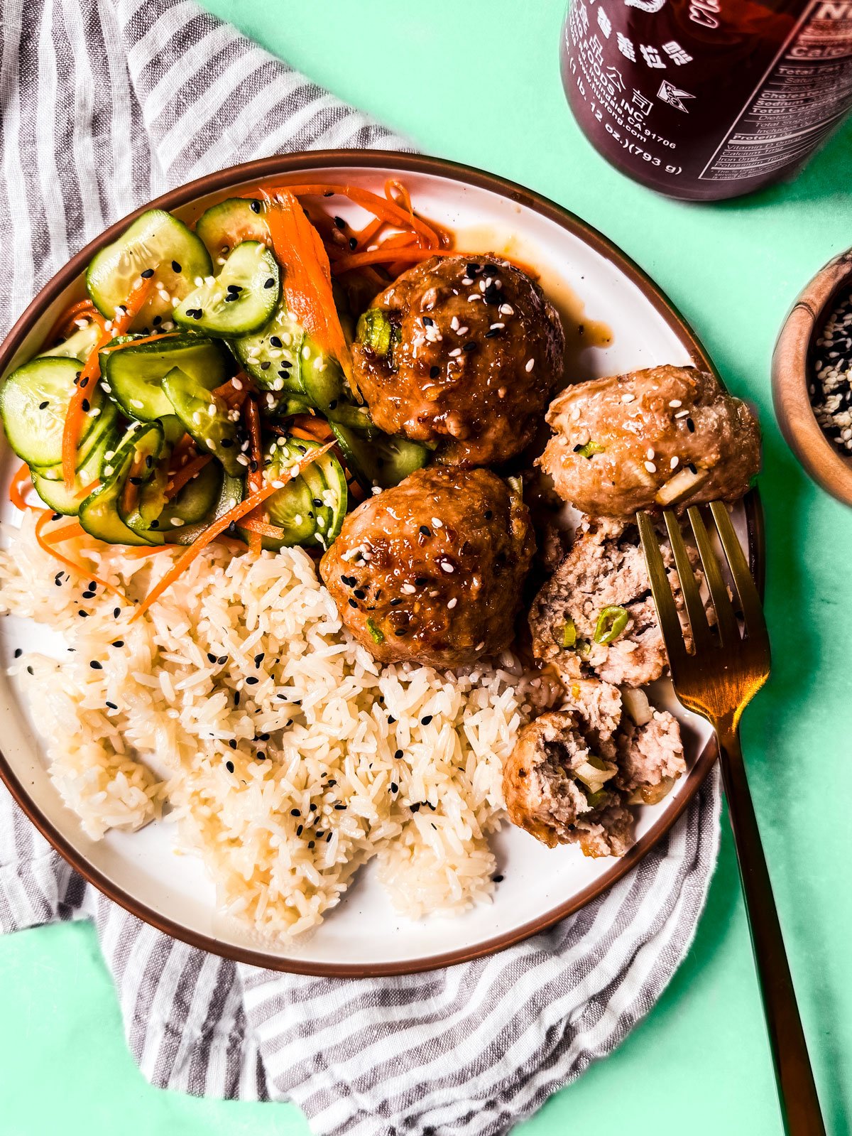 Baked turkey meatballs in honey glaze on a plate with rice and cucumber salad.