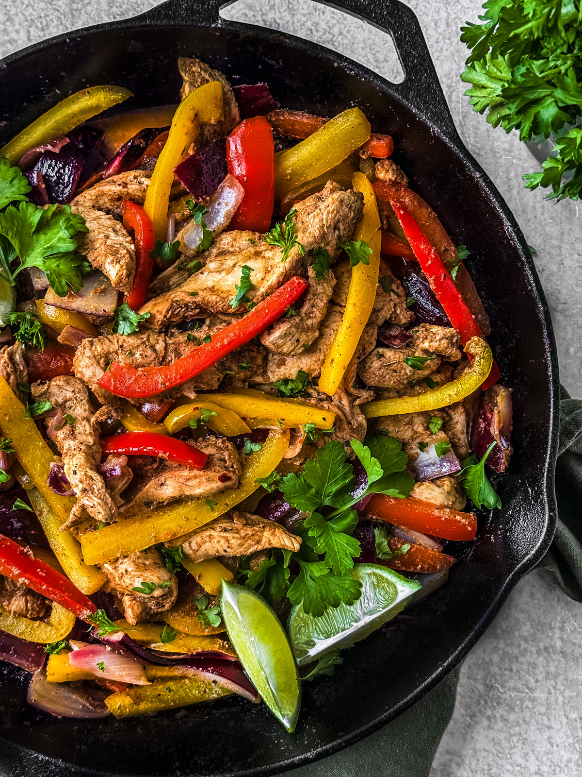 Chicken and peppers in a cast iron skillet with lime wedges.
