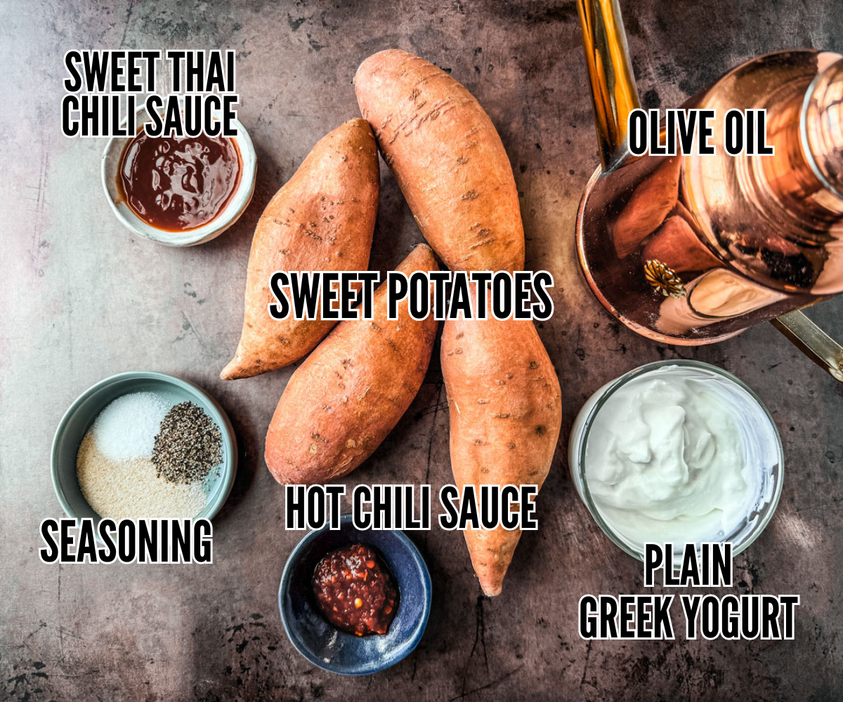 Sweet potatoes on a dark background with olive oil canister and small bowls of sweet thai chili sauce, seasoning, hot chili sauce, and Greek yogurt.