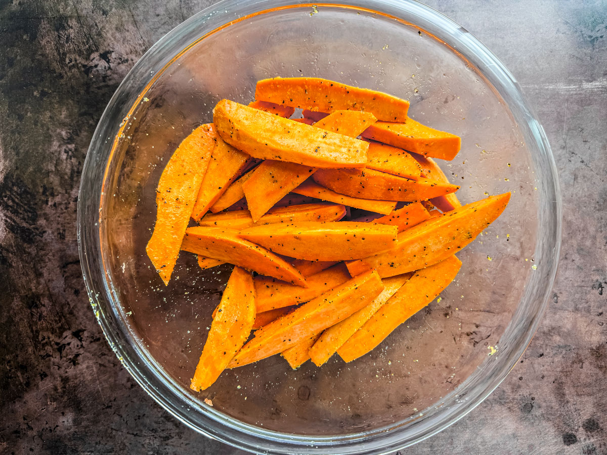 Sweet potato wedges in a mixing bowl with seasoning.