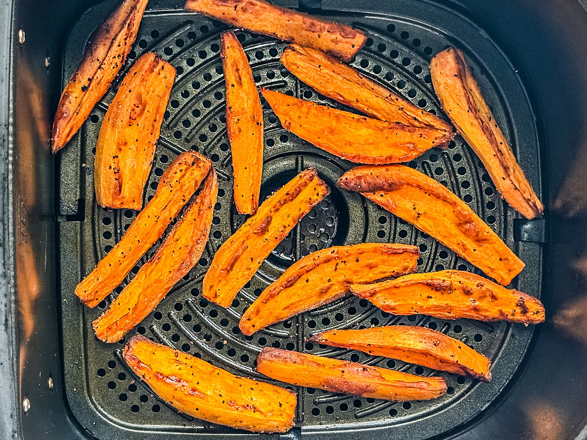 Cooked crispy sweet potato wedges in an air fryer basket.