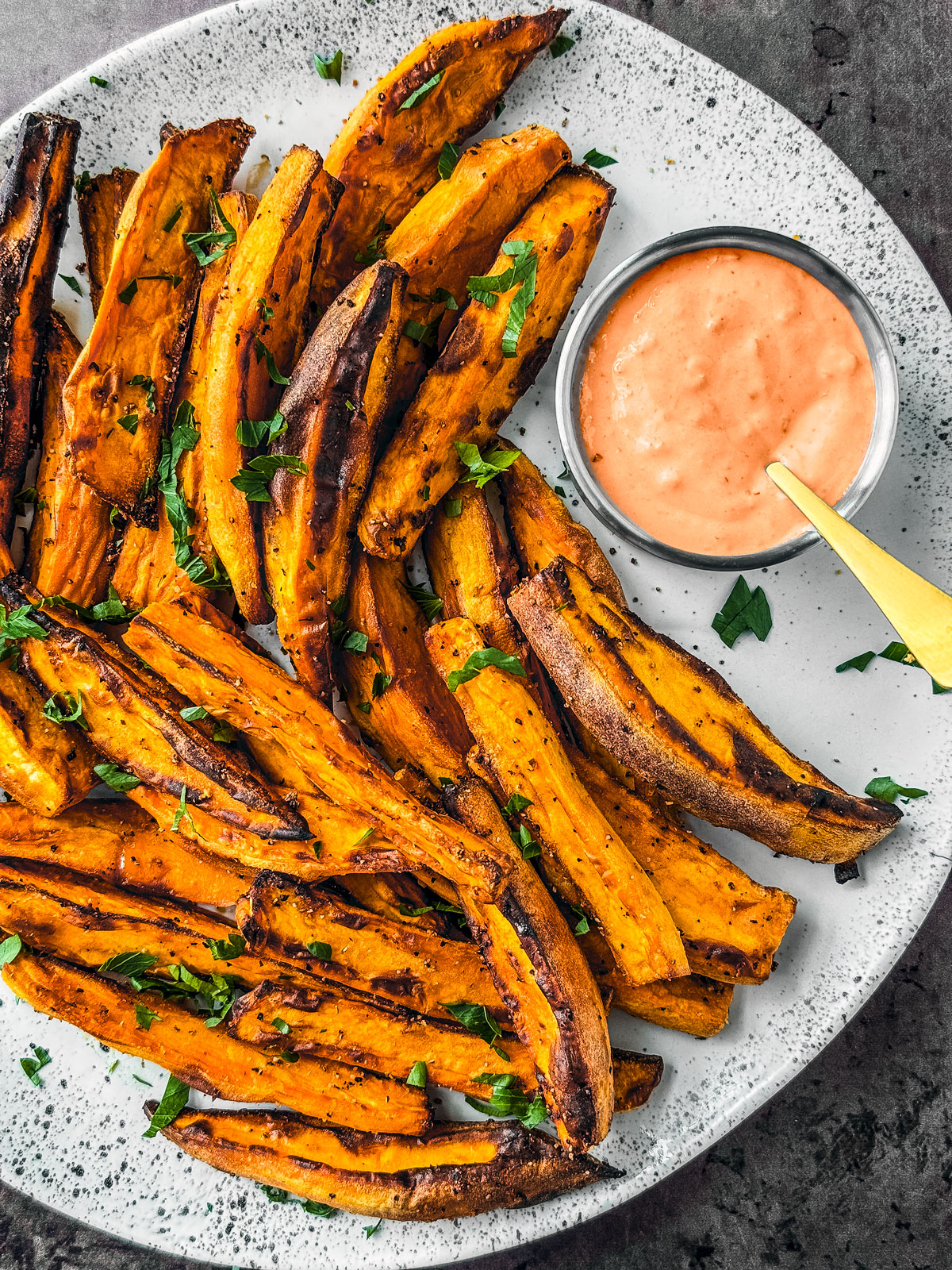 Sweet potato wedges on a platter with a dish of sweet and spicy yogurt dipping sauce.